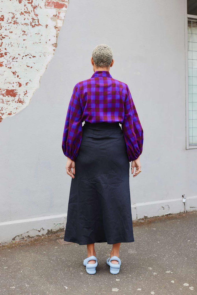Collective Closets model from behind wearing black linen drawstring skirt and purple plaid shirt